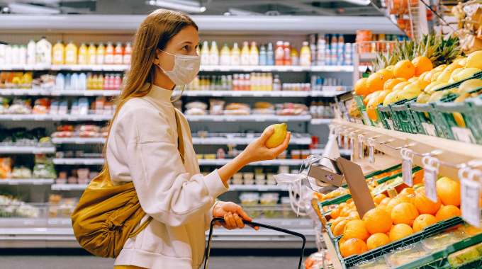Woman budget-shopping for groceries with mask on